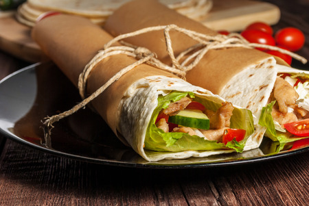 Mexican tortilla wrap with meat and vegetables on wood table