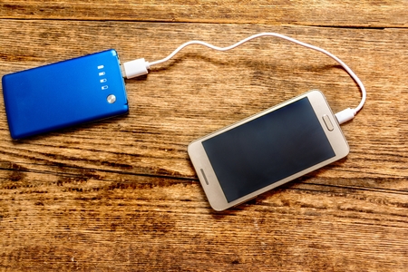 Mobile phone charging by power bank on wood tableの写真素材