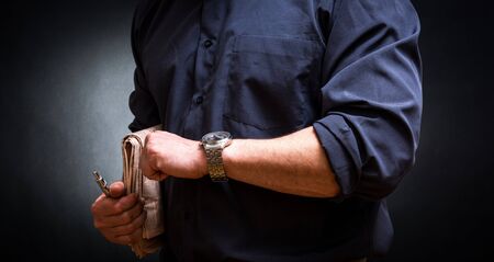Business man  with newspaper looking at watch  dark backgroundの写真素材