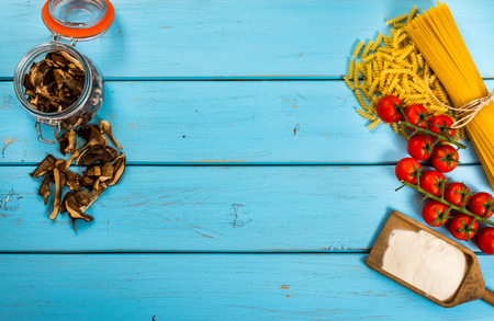 Food or cooking backgroud with pasta, tomato, spaghetti, penne, mushroom and flour on blue wood table.Top view.Copy space.の写真素材