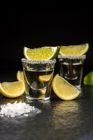 Mexican alcoholic drink tequila with salt and lemon or lime on black stone tableの写真素材