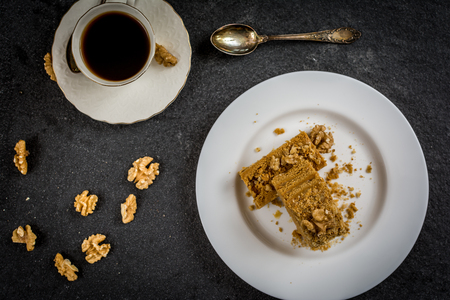 Traditional dessert honeycake with walnuts on white plate and coffee top viewの写真素材