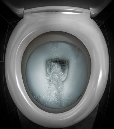 Water flushing into the white ceramic toilet bowl in the dark restroomの写真素材