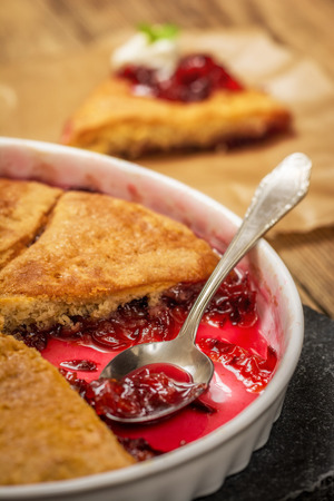 Homemade baked dessert plum cobbler with whipped cream on wood tableの写真素材