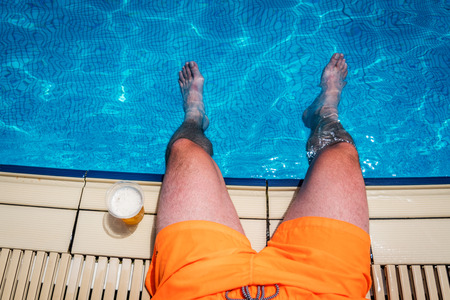 Man sitting near simming pool with plastic bottle with draft beer in sunny day in summerの写真素材