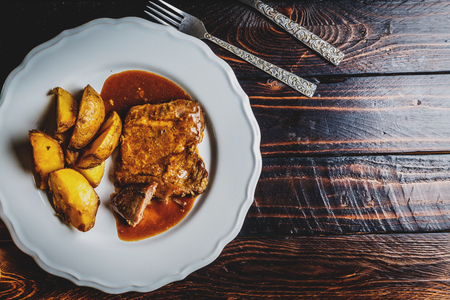 Grilled pork steak and fried potatoes on white plate on dark wood tableの写真素材