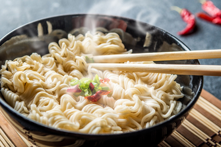 Black bowl of asian instant noodles with hot water and red chili peppers and green onionの写真素材
