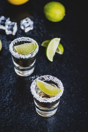 Mexican traditional  Tequila with lemon, lime,salt and ice cube on dark stone table tableの写真素材