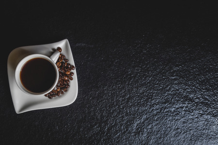 White cup of coffee and coffee beans on black stone table top viewの写真素材