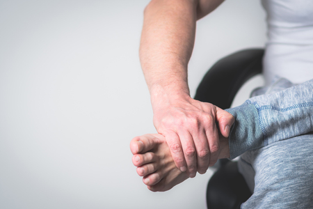 Causian man holds hands to his painful feet, pain in footの写真素材