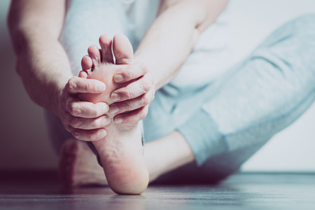 Causian man holds hands to his painful feet, pain in foot