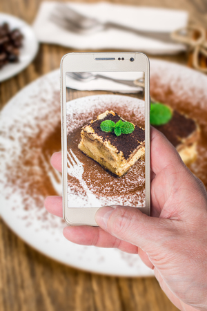 Man taking photo of Traditional italian dessert tiramisu cream on wood tableの写真素材