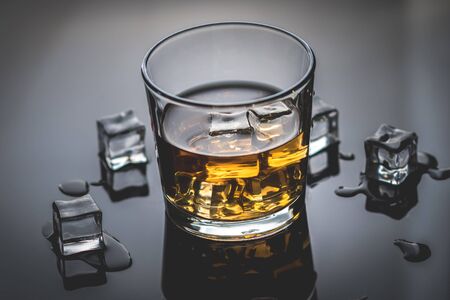Whisky, whiskey or bourbon in glass with ice cubes on black reflection backgroundの写真素材