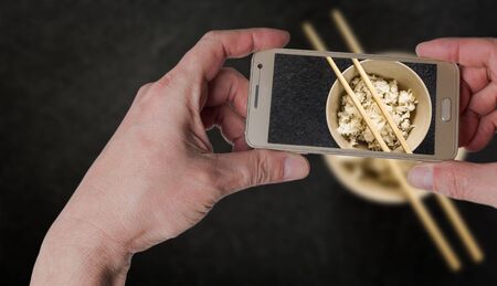 Man taking photo of Asian rice in white bowl on dark backgroundの写真素材