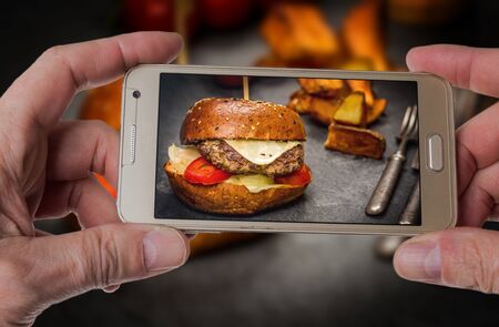 Man taking photo of Traditional Cheeseburger with beef meat and fried potato