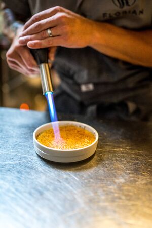 Cook make Traditional dessert Creme brulee with flowers in white bowl