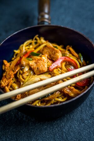 Asian noodles with chicken meat and vegetables on black stone tableの写真素材
