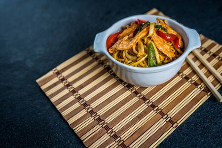 Asian noodles with chicken meat and vegetables on black stone tableの写真素材
