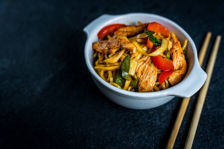 Asian noodles with chicken meat and vegetables on black stone tableの写真素材