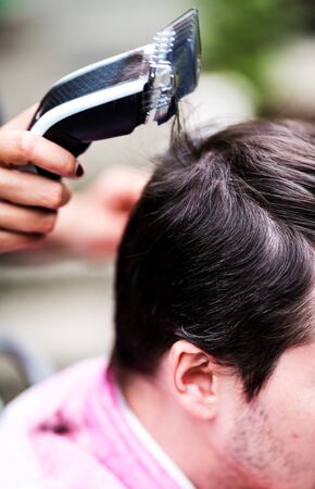 Woman cutting men hair in hairdresser shop with hair clippersの写真素材