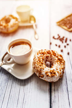 White donut with chocolate sprinkle and cup of coffee on wood tableの写真素材