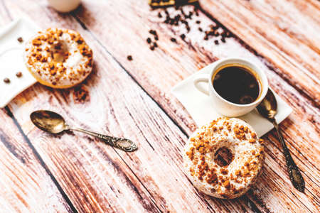 White donut with chocolate sprinkle and cup of coffee on wood table