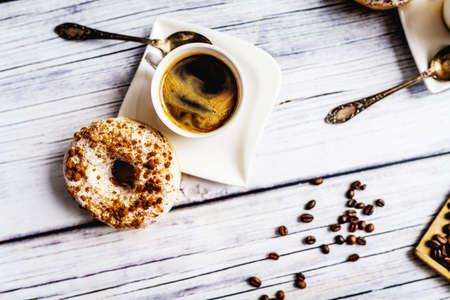 White donut with chocolate sprinkle and cup of coffee on wood tableの写真素材