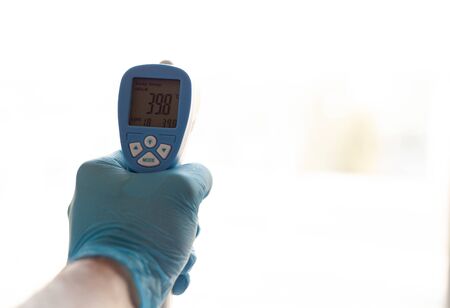 a doctor in a blue gloves, holding an electronic thermometer with indicators of high body temperature on a white backgroundの写真素材