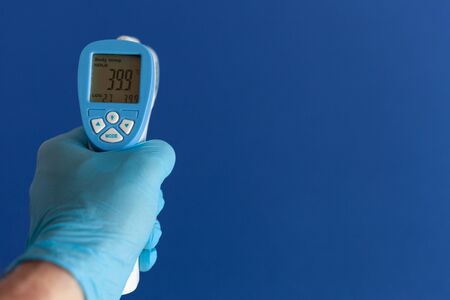 a doctor in a blue gloves, holding an electronic thermometer with indicators of high body...