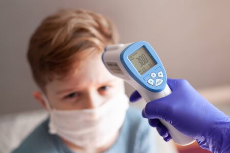 Measures the body temperature of a boy in a medical mask with an electronic thermometer.