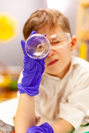 the child the boy stayed at home, conducts experiments on a white table, behind him on the wall is a white board for magnets and markers, activities with the child at home, educational activities at home for childrenの写真素材