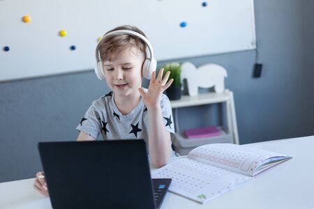 Boy is engaged at home online school, learning in isolationA boy writing down in a notebook was taken out of a laptop. The child is remotely engaged using a laptop. Distance Learning during Quarantine Conceptの写真素材