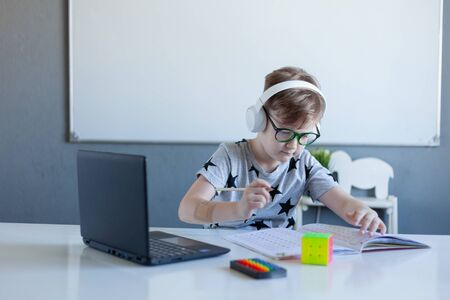 Boy is engaged at home online school, learning in isolationA boy writing down in a notebook was...