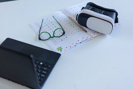 laptop, virtual reality glasses, copybook are on the table, desk of a modern schoolboy, concept of...