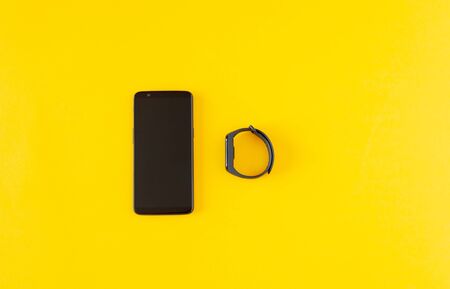 Smartphone and smart bracelet on a yellow background, measuring body parameters for health. Modern...
