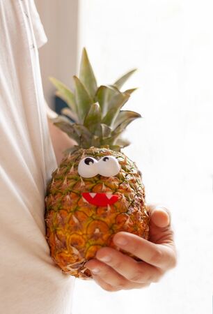 man holds pineapple in his hands with toy eyes and a smile, the concept of vegetarianism, veganの写真素材