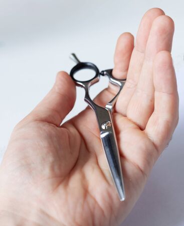 hand holds hairdressing scissors close-up, on a white light background, barbershop barber shop concept, hair care, hairdresser stylistの写真素材