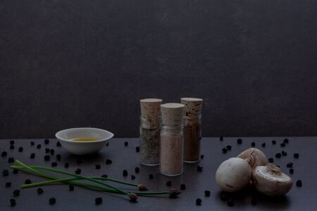 jars with spices, olive oil, stalks of greens and dried blueberries, cooking concept, granite dark...