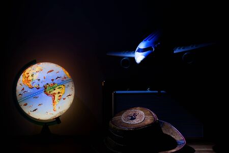 backlit globe lamp, airplane suitcases and hat in the dark, adventure concept