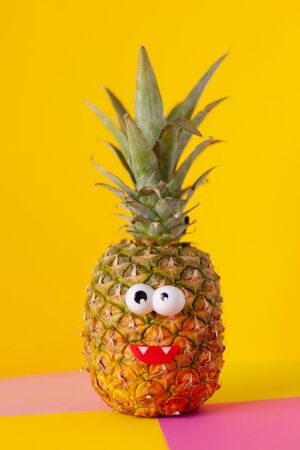 pineapple fruit with funny eyes on a yellow pink backgroundの写真素材
