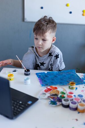 boy paints, online drawing classes, gray Tshirt with stars, laptop on the tableの写真素材