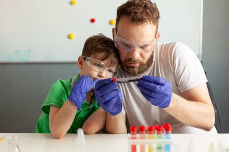 a man and a boy carefully examine a test tube with dark liquid, sit at a table in a laboratoryの写真素材