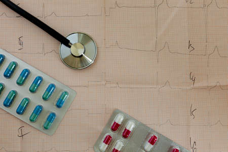 medical statoscope and tablets of different colors in blisters on a table with a cardiologist lies...