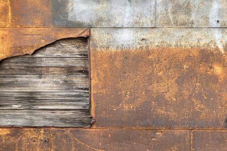 a rusted steel metal wall with exposed rotten wood board