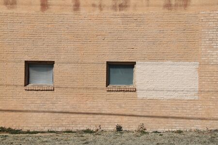 a pair of square vintage windows on the facade of a brown brick wall warehouse building