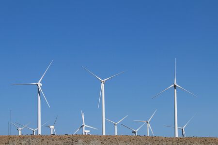 a hillside view wind farm with bright white turbines and blue sky