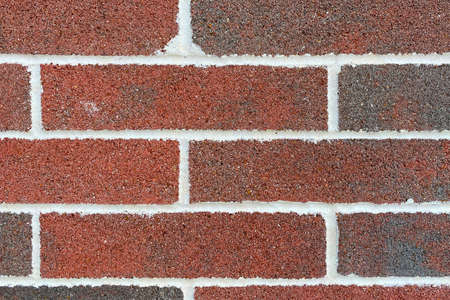 a closeup view of a red and brown brick wall with white grout displaying detail weathered horizontal...