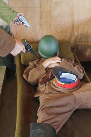 Soldier sleeping on army bed with 2 people pointing gun at himの写真素材