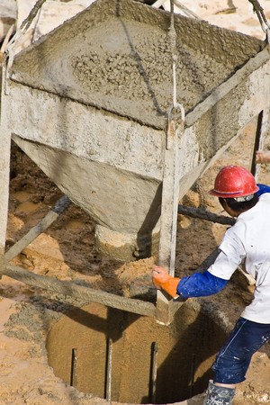 Construction worker pouring concrete from container lifted by crane (1)