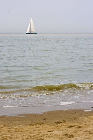 Sunny beach with sailing boat in distanceの写真素材